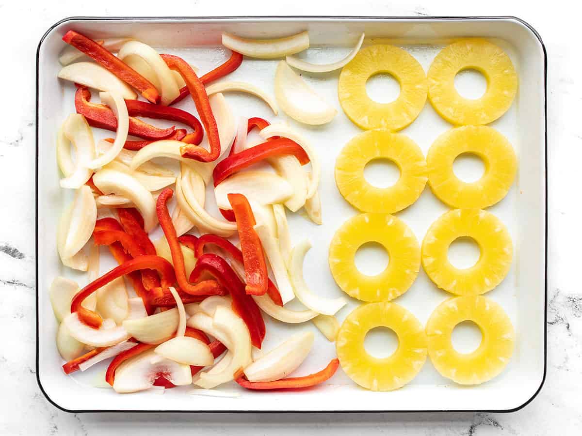 Pineapple slices on a baking sheet with the peppers and onions