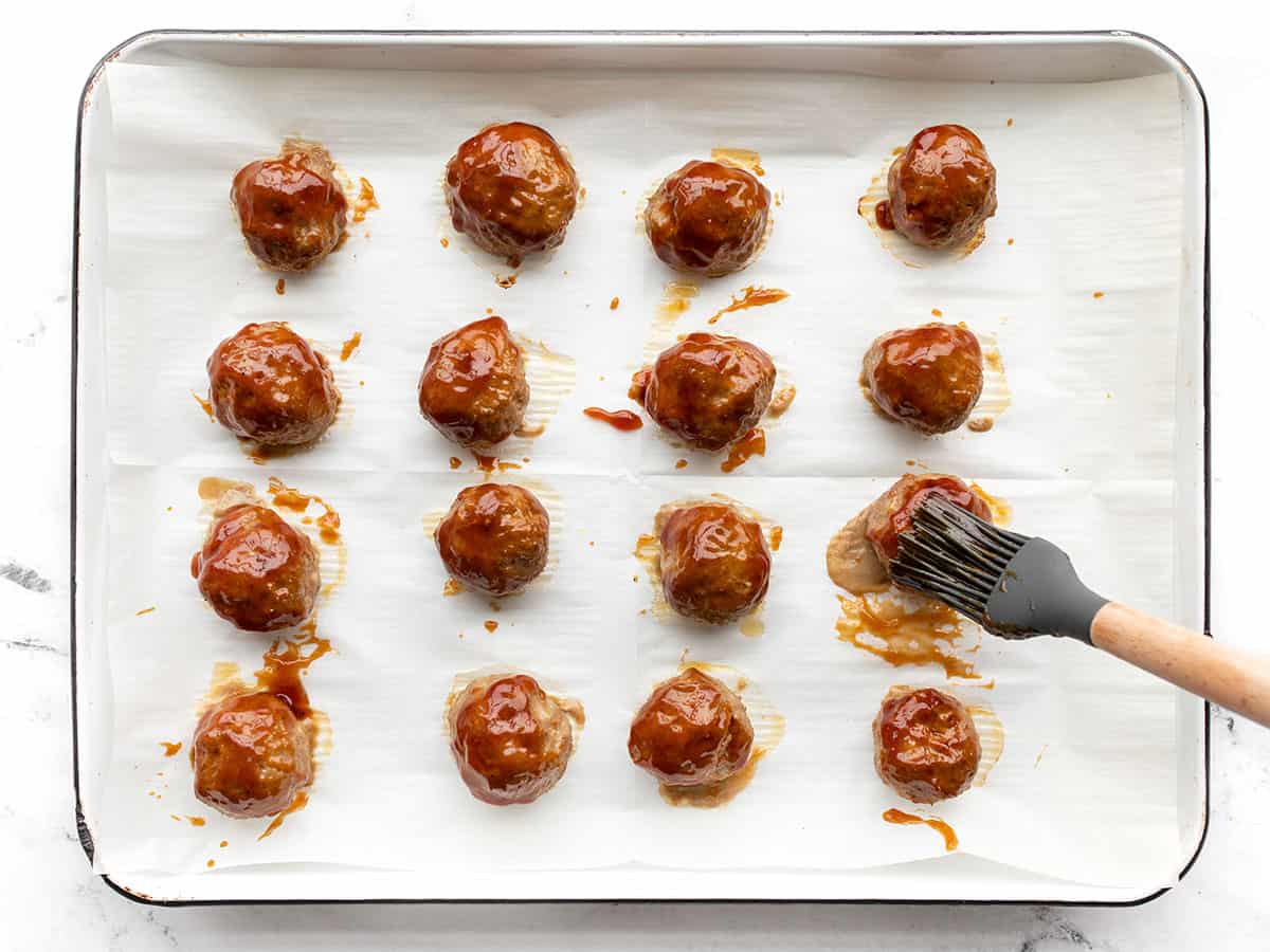 BBQ sauce being brushed onto the meatballs