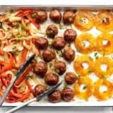Overhead view of sheet pan with bbq meatballs, pineapple, peppers, and onions, tongs on the side