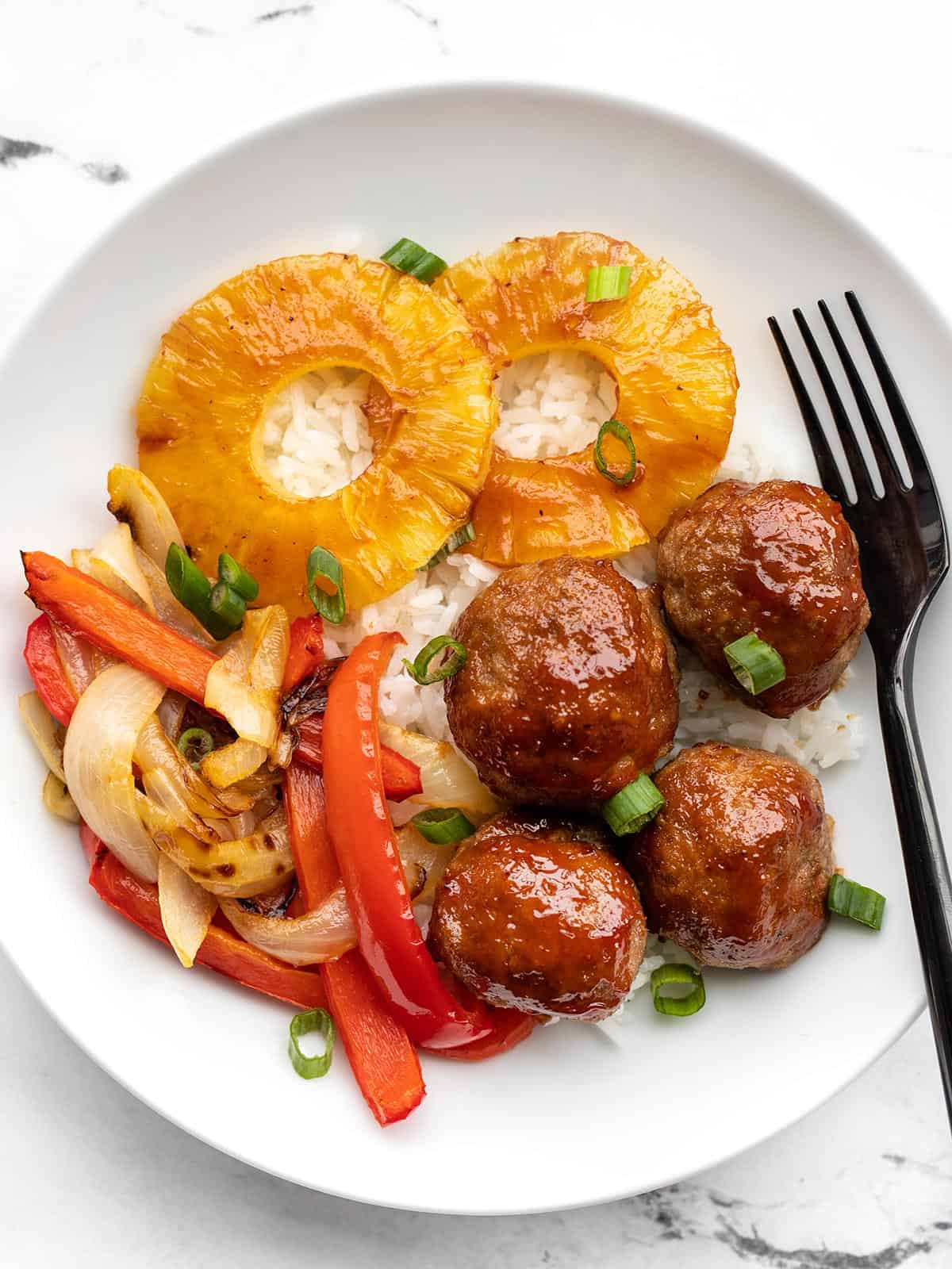 A bowl with rice, sheet pan BBQ meatballs, roasted peppers and onions, and pineapple slices.