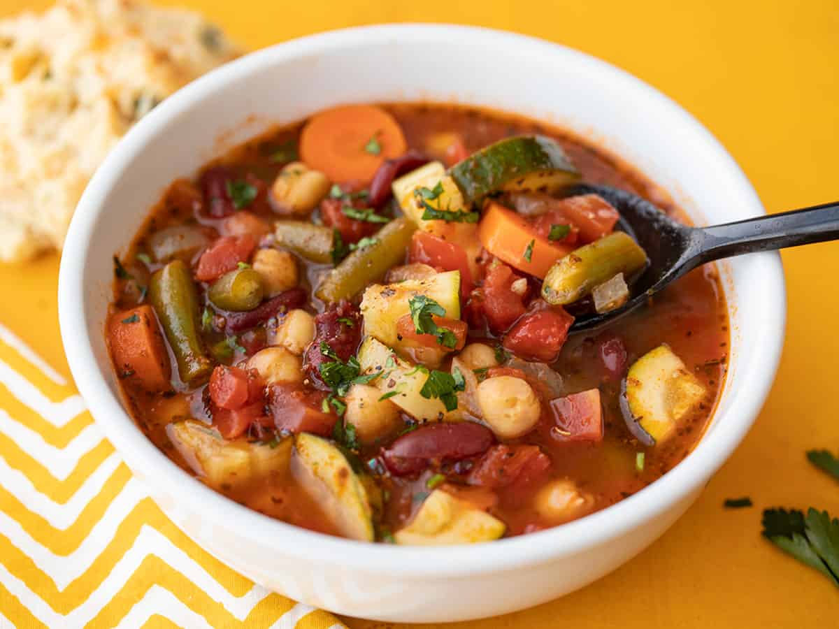 Front view of a bowl full of vegetarian minestrone with a spoon lifting a bite