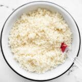 Overhead view of a bowl of riced cauliflower with a red spatula in the side