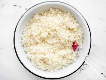 Overhead view of a bowl of riced cauliflower with a red spatula in the side