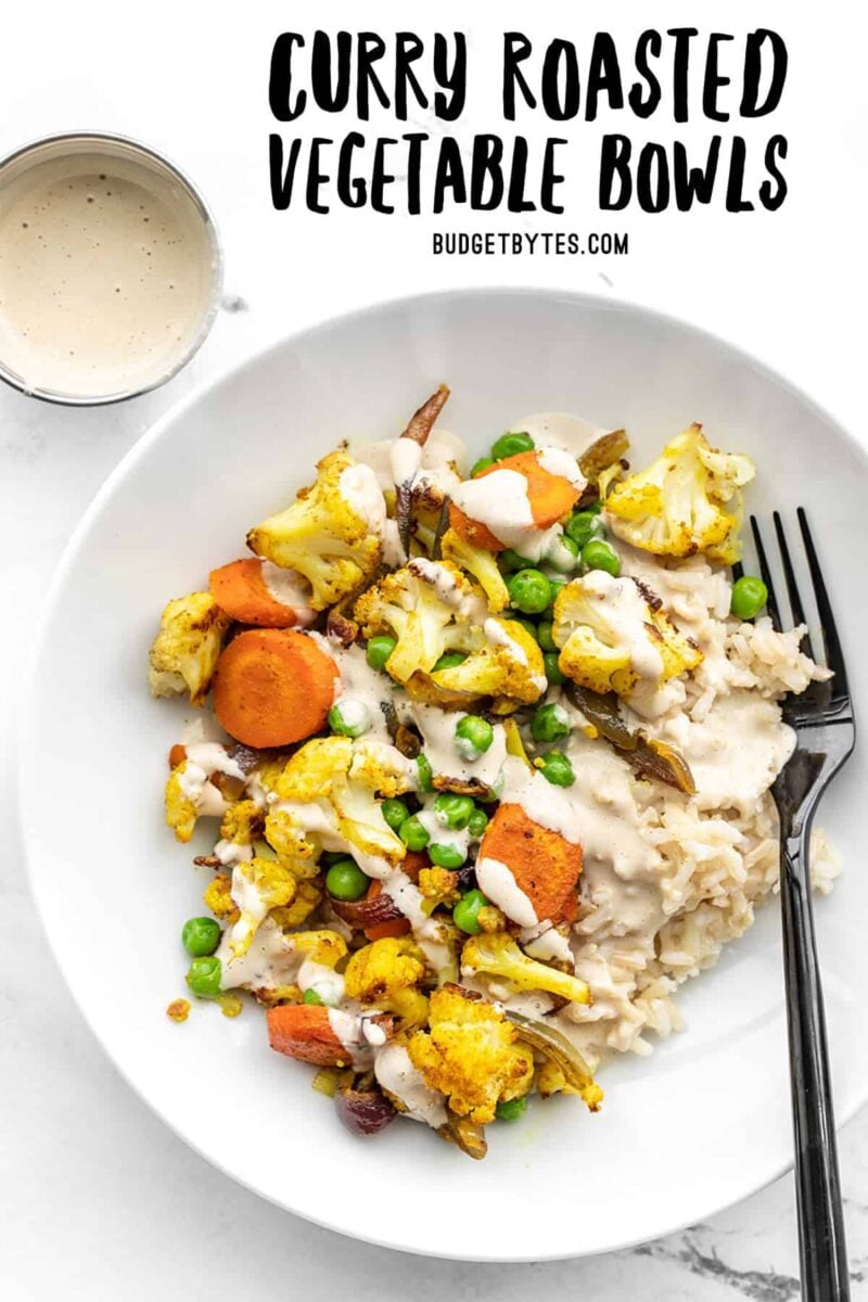 Overhead of curry roasted vegetable bowls with a fork in the side and a small dish of dressing on the left