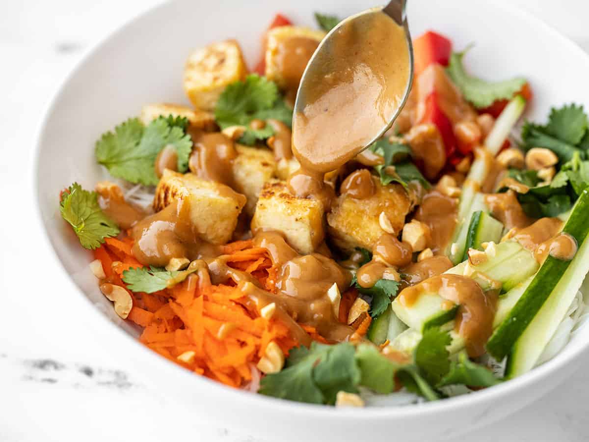 close up side view of peanut lime dressing being drizzled over a peanut tofu noodle bowl