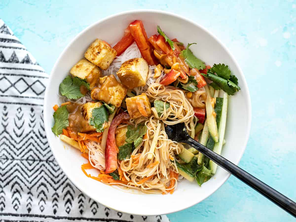 Half-stirred peanut tofu noodle bowl with a fork in the center