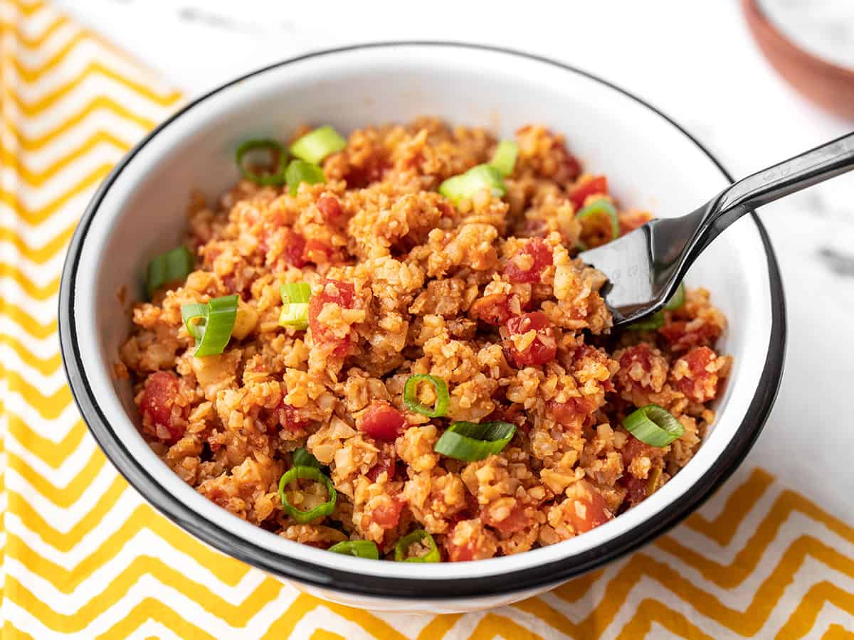 Side view of a fork picking up some southwest cauliflower rice out of a bowl