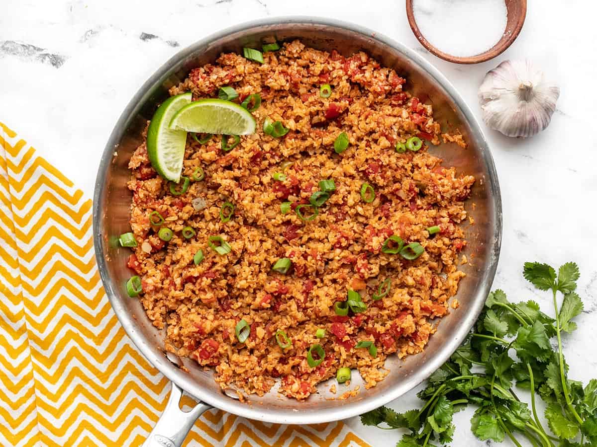 Overhead view of a skillet full of southwest cauliflower rice with a bowl of salt and cilantro on the side