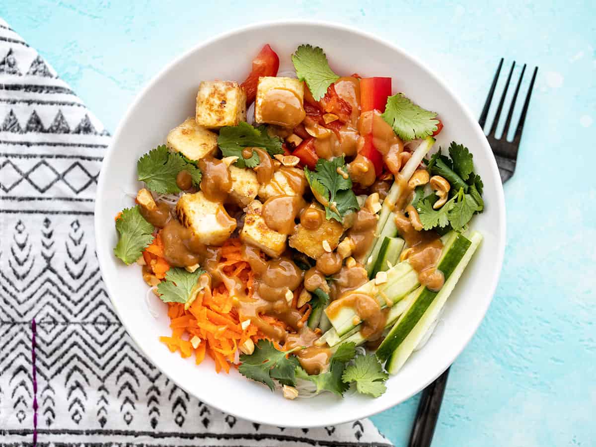 Overhead view of a peanut tofu noodle bowl with a black fork on the side