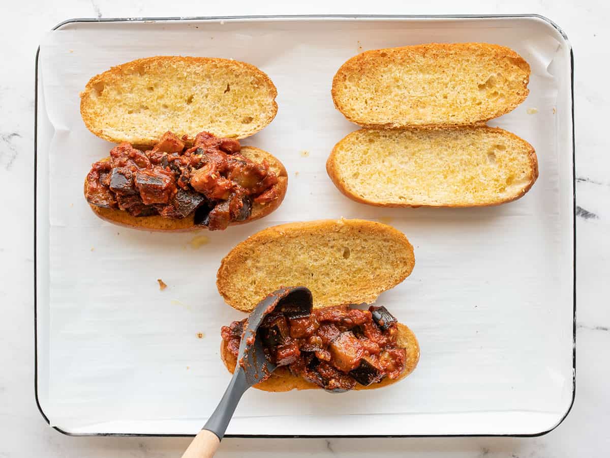 Eggplant mixture being spooned onto toasted rolls