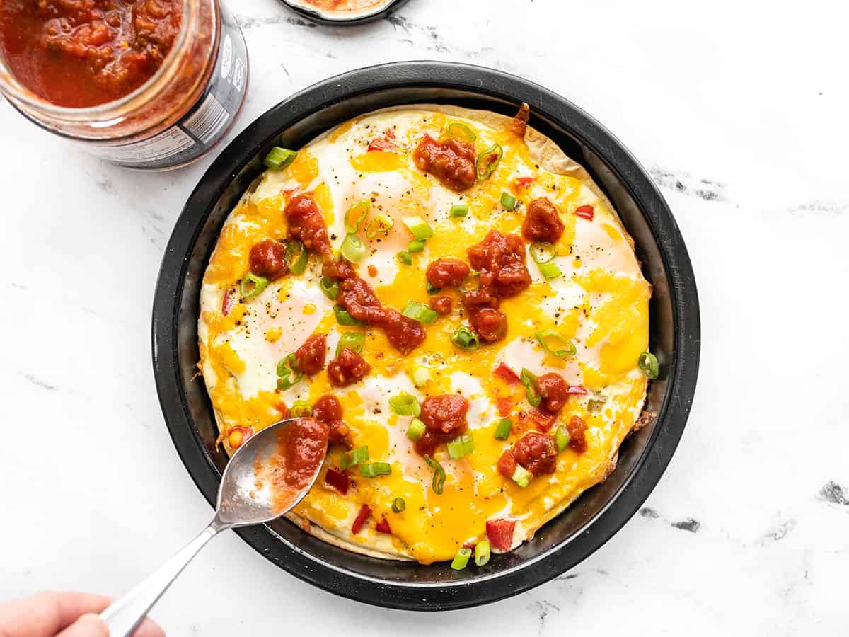 Salsa being spooned on top of the tortilla baked eggs