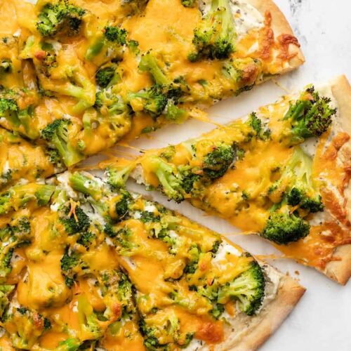 One slice of broccoli cheddar pizza being pulled from the pie