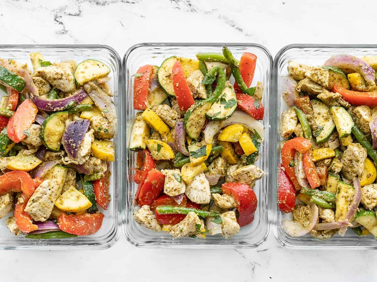 Pesto chicken and vegetables in glass meal prep containers lined up side by side