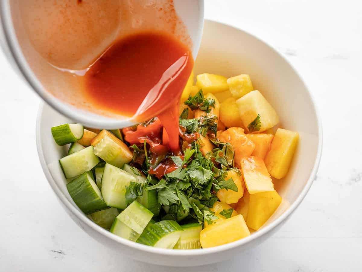 Dressing being poured over cucumbers and pineapple