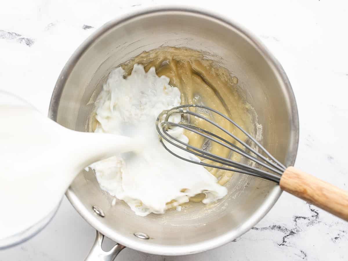 milk being poured into the pot with butter and flour