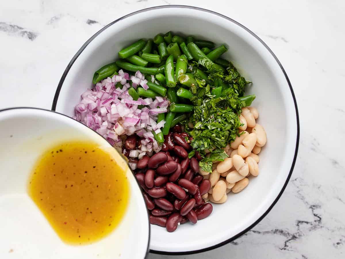 dressing being poured over salad ingredients in the bowl