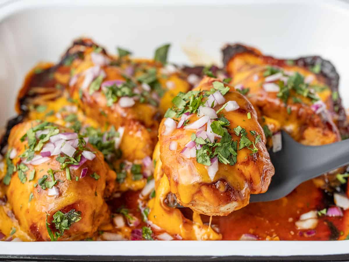 bbq cheddar baked chicken being lifted out of the baking dish, viewed from the side