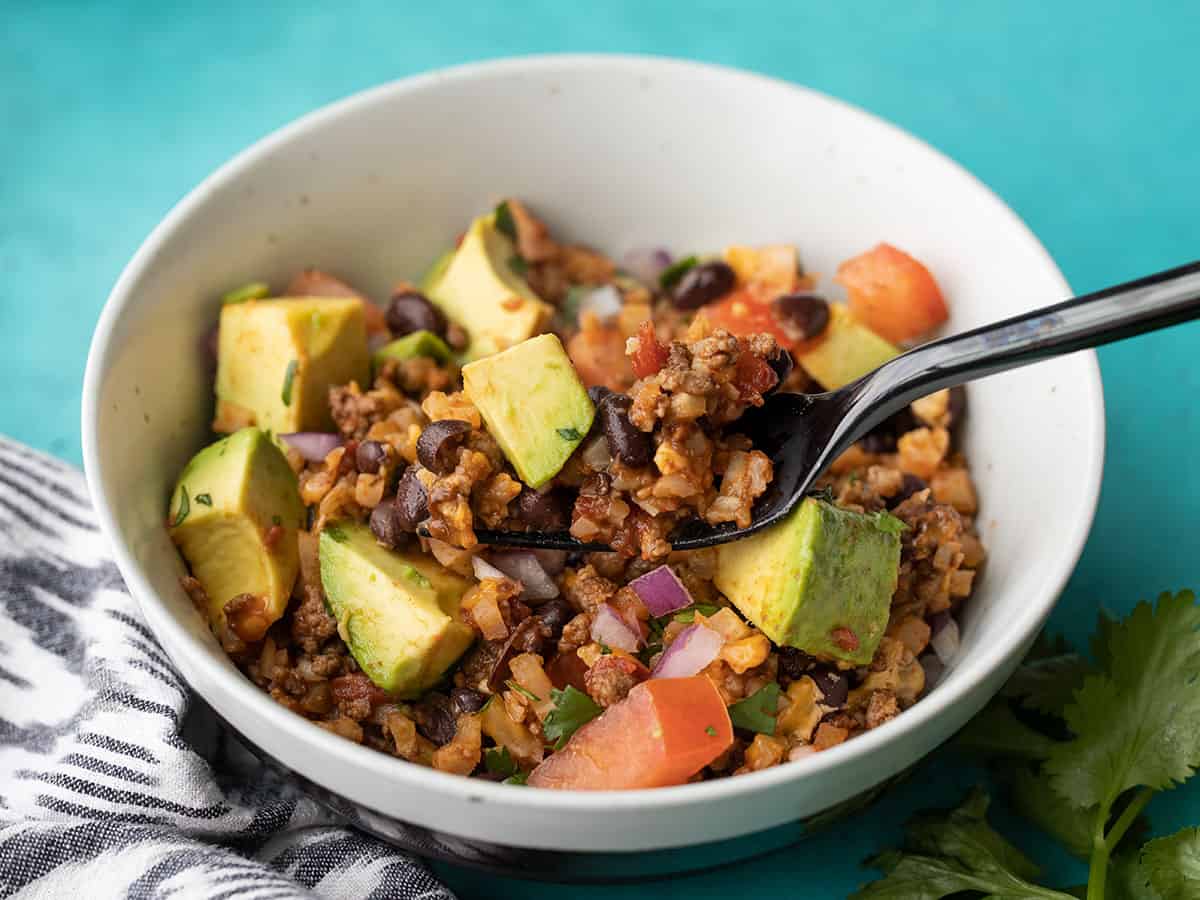 A fork lifting a bite of beef and cauliflower taco skillet out of a bowl