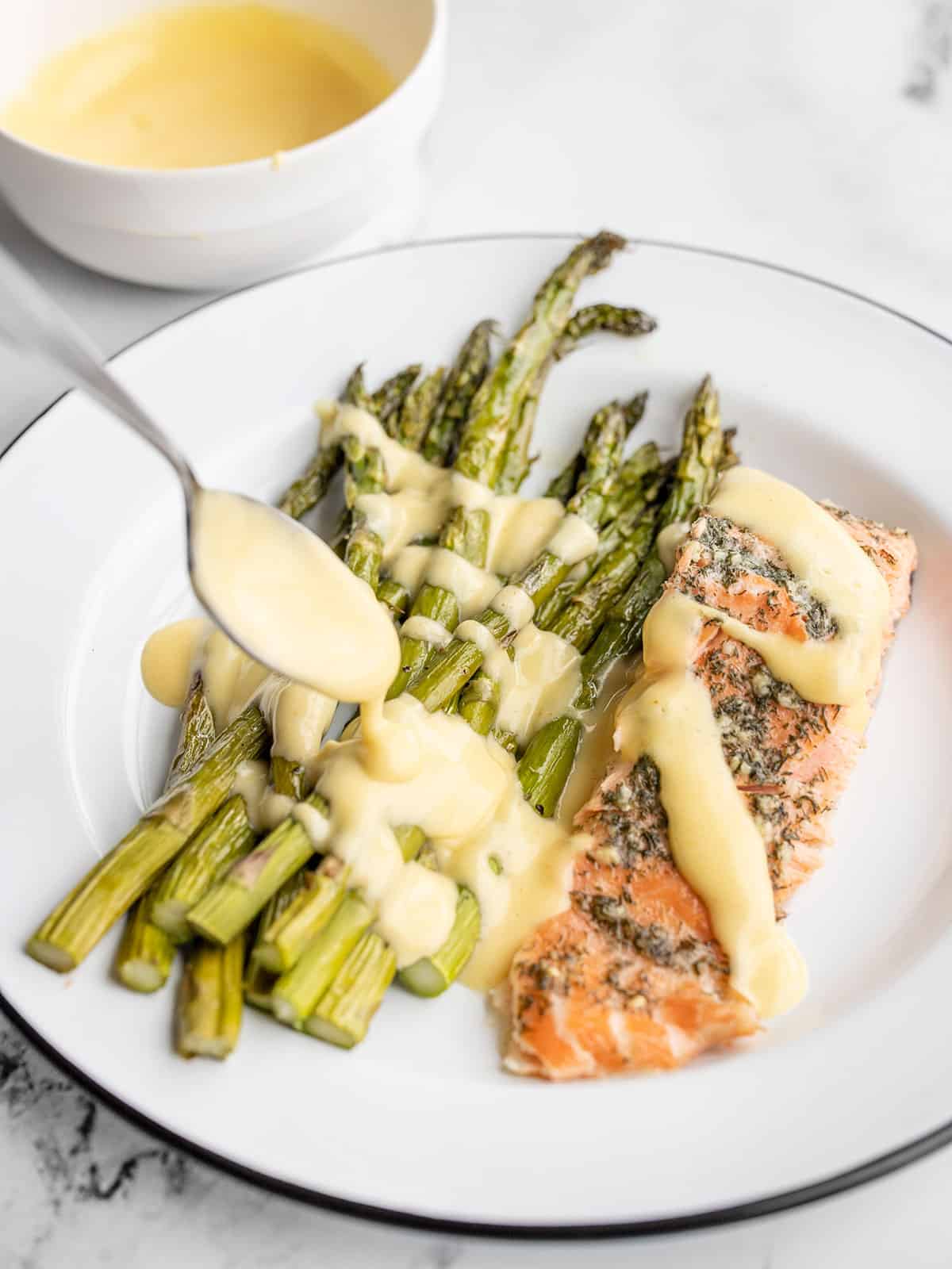 Hollandaise sauce being drizzled over asparagus and salmon