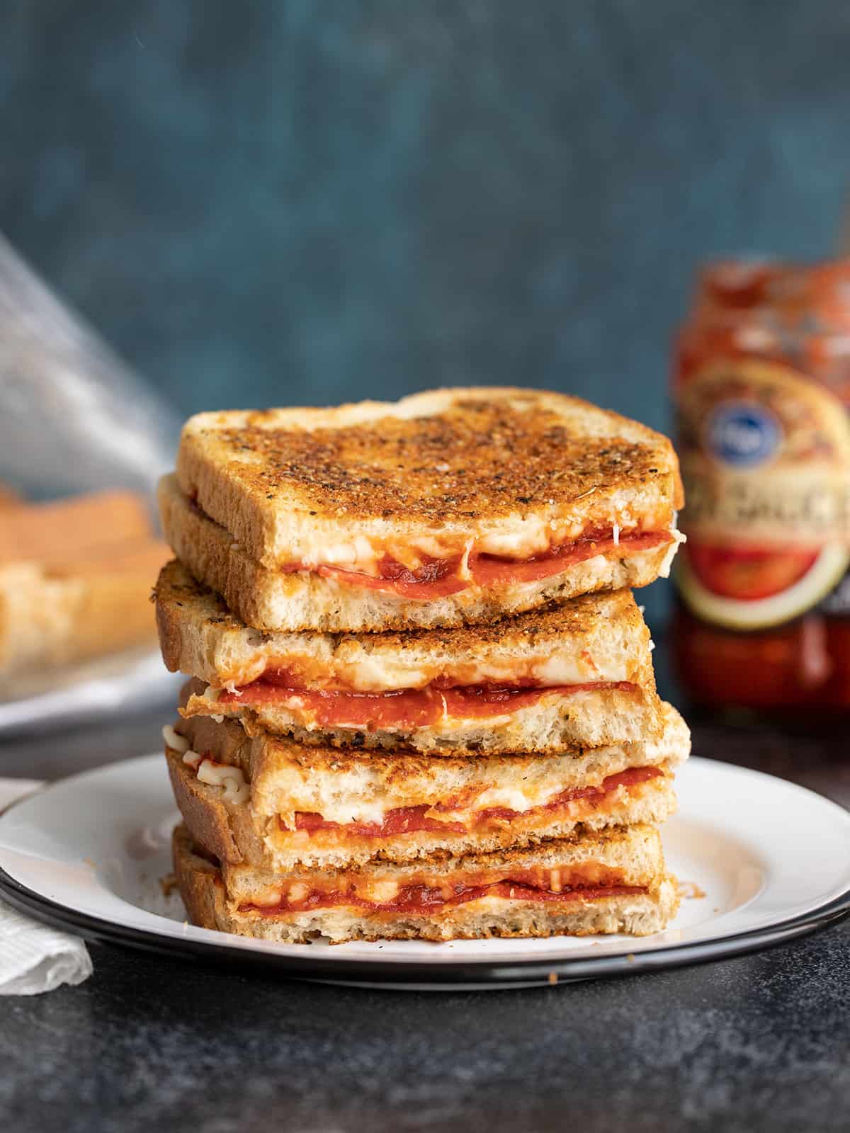 A stack of pizza melts cut in half on a plate against a blue background