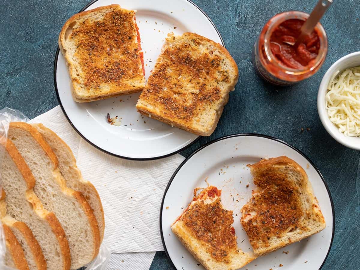 Two pizza melts on a plates with bread, sauce, and cheese on the sides