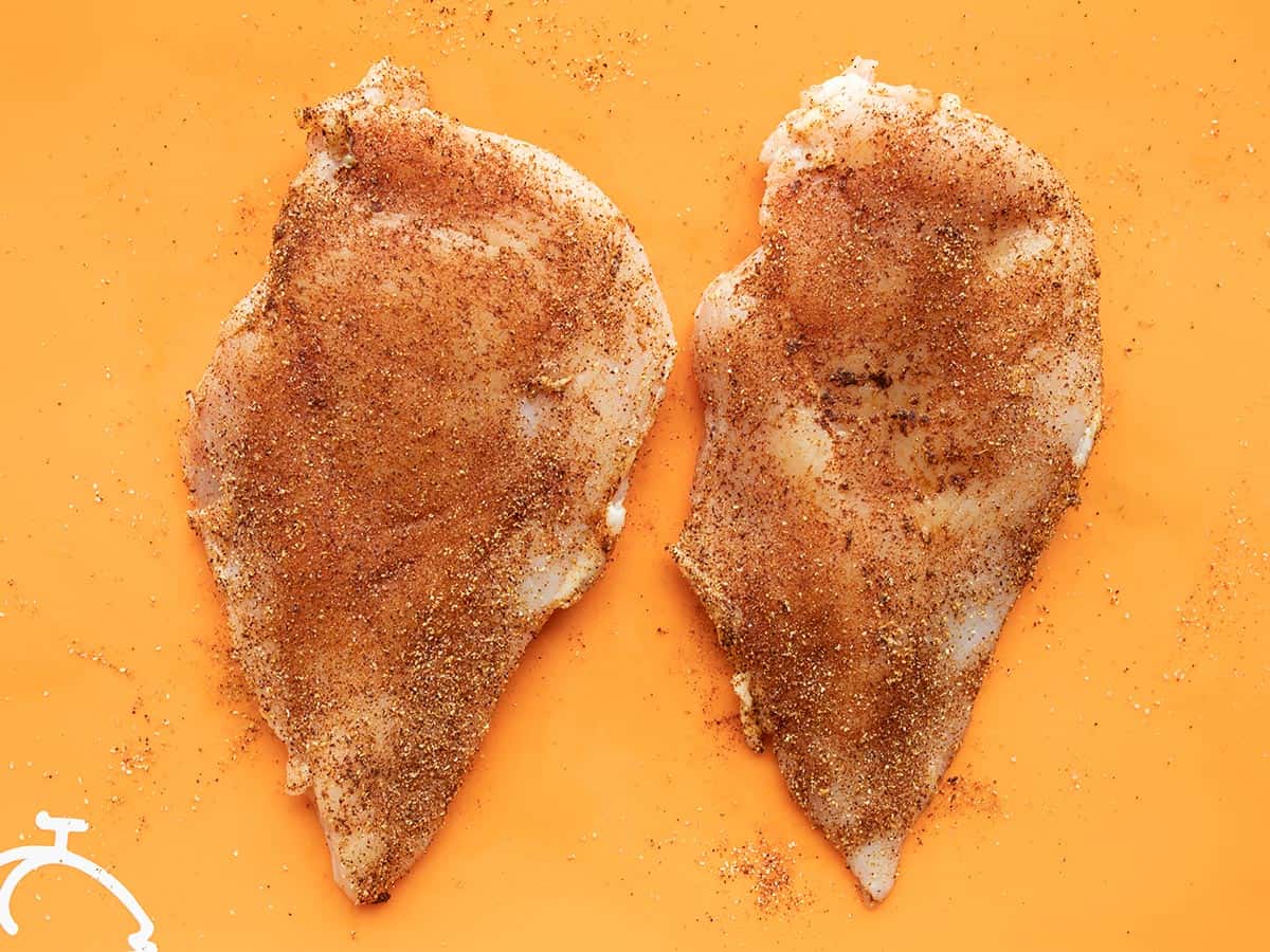 Seasoned chicken breast on an orange cutting board