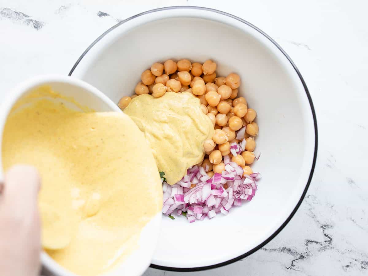 curry dressing being poured over salad ingredients in the bowl