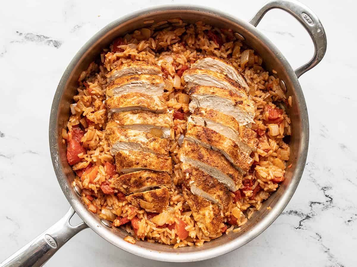 Sliced chicken on top of stirred rice in the skillet