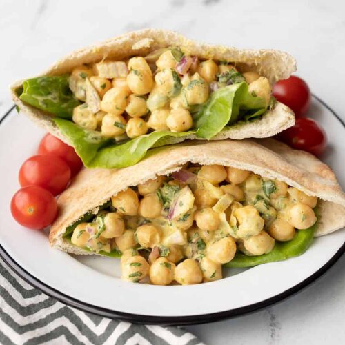 two pita pockets stuffed with curry chickpea salad on a plate with grape tomatoes