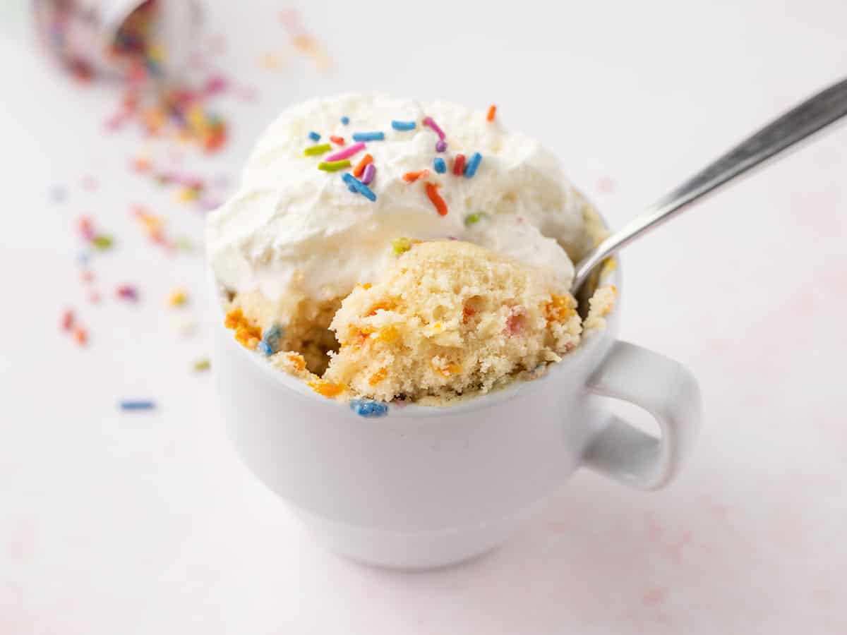 a spoon lifting a bite of the funfetti mug cake out of the mug