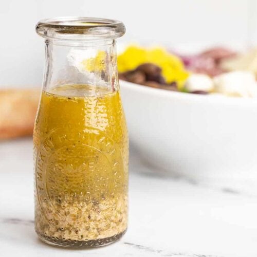 Italian dressing in a glass carafe in front of a bowl of salad