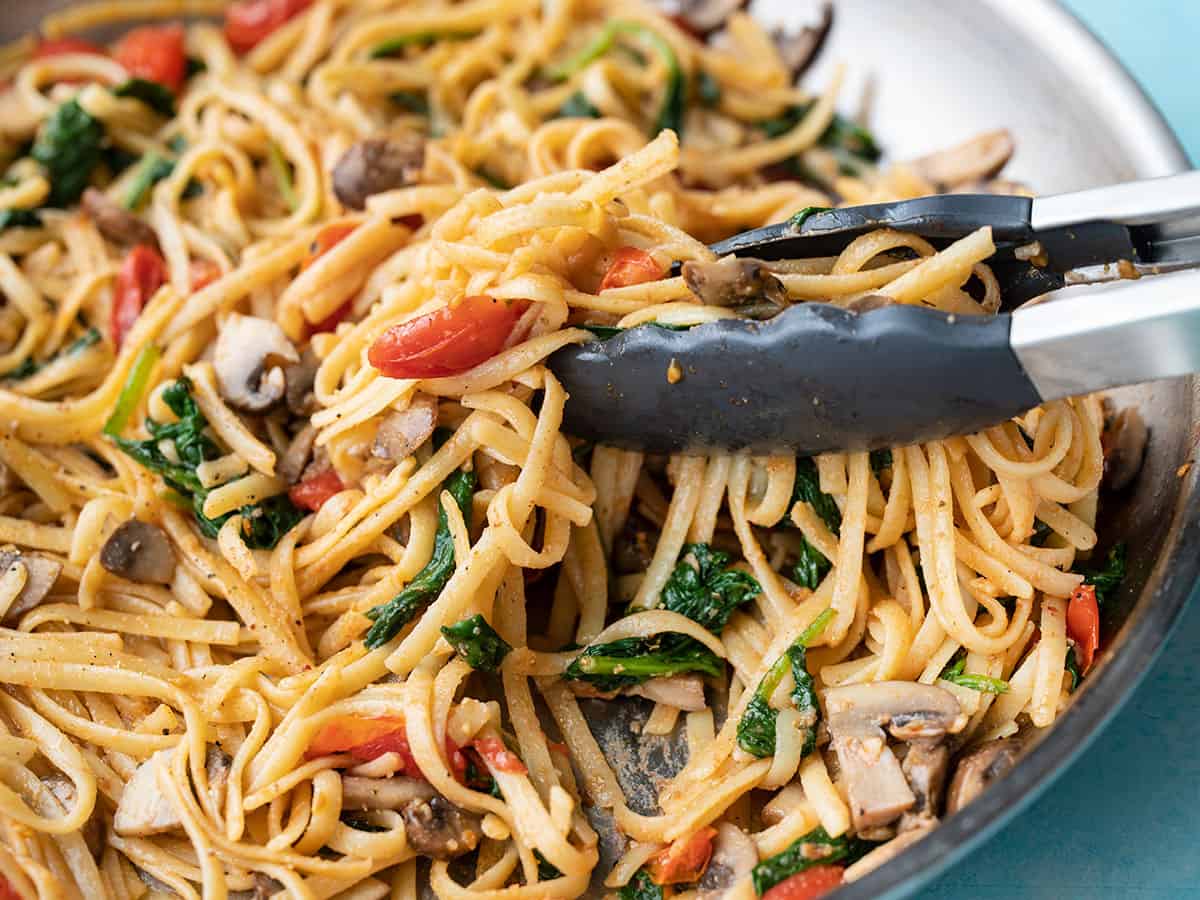 Side view of pasta in the skillet being picked up by tongs