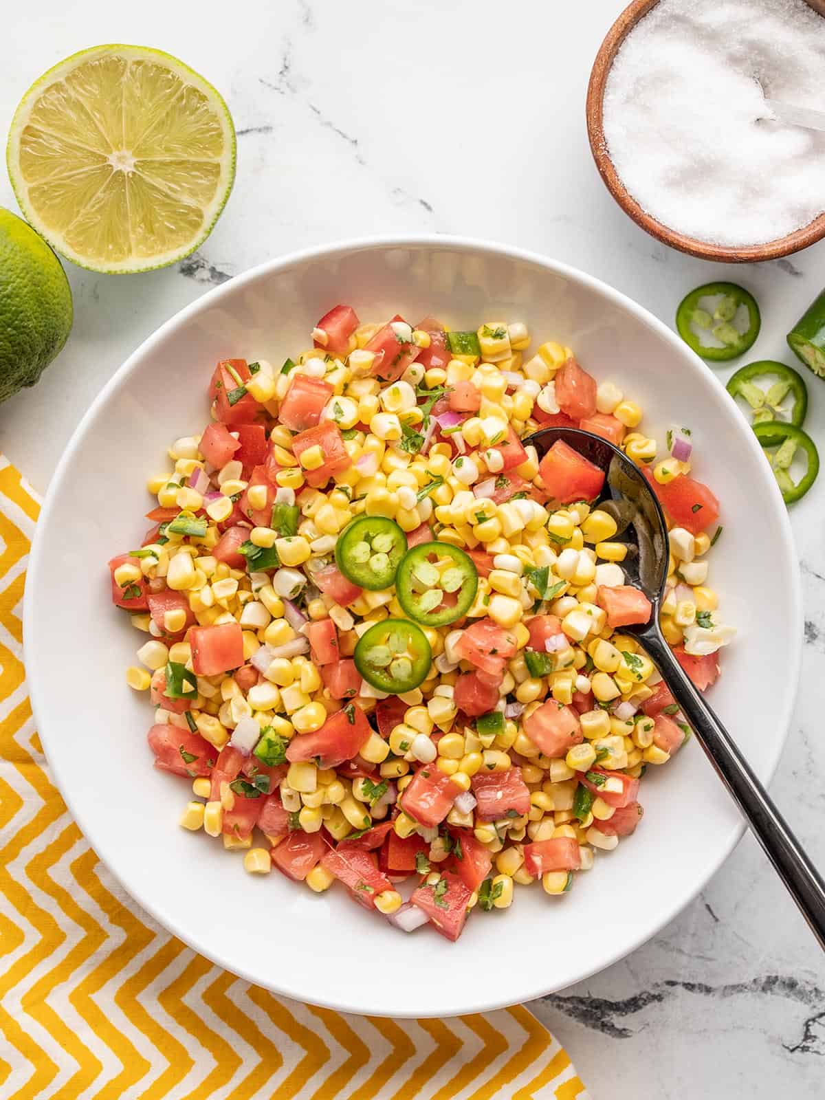 Overhead view of a bowl of sweet corn salsa with lime and salt on the side