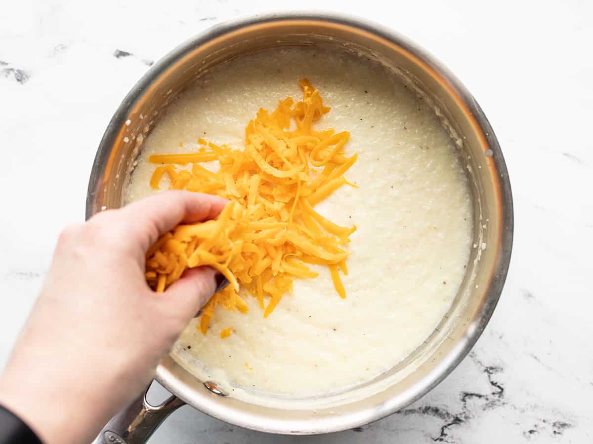 Shredded cheddar being added to grits