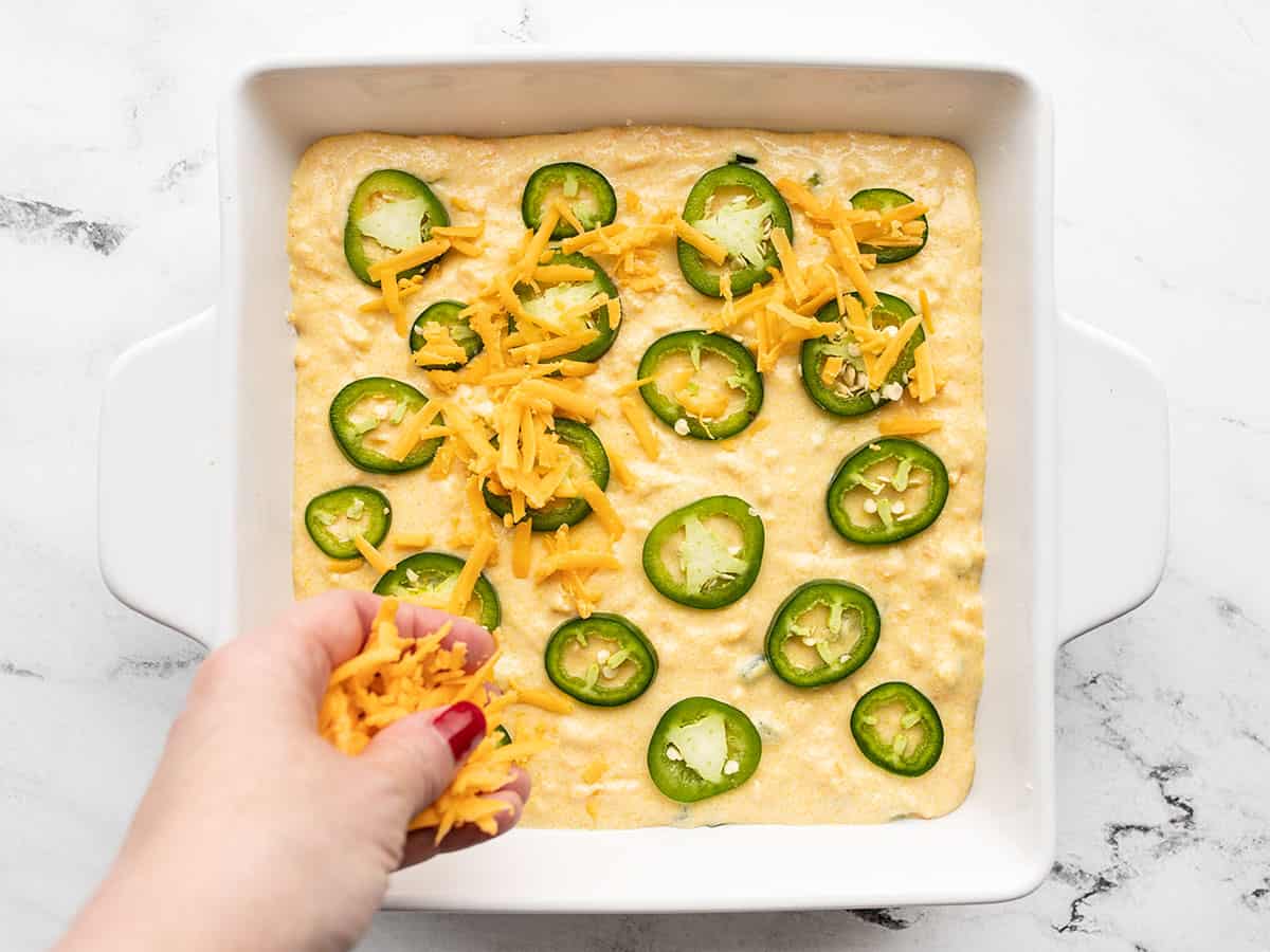 cheddar being sprinkled on top of cornbread batter in the baking dish