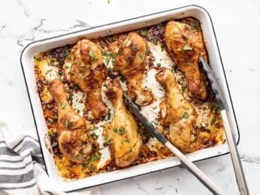 Oven roasted chicken drumsticks on a baking sheet with tongs