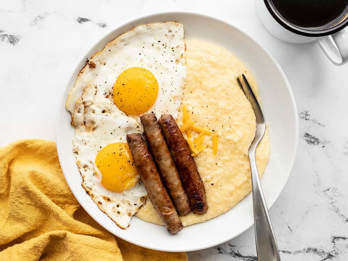 cheese grits in a bowl topped with fried eggs and breakfast sausage