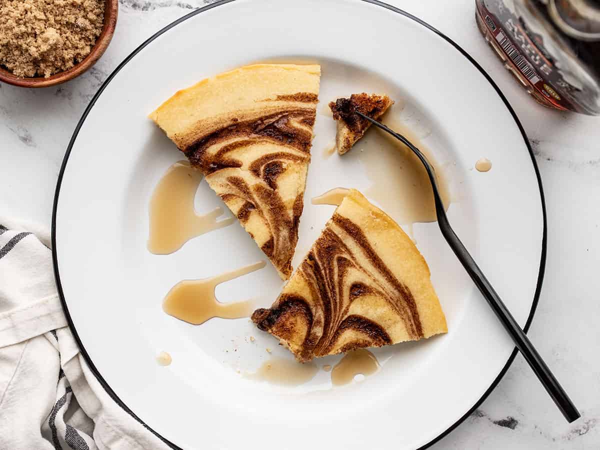 Two slices of cinnamon swirl oven pancake on a plate with a fork and maple syrup