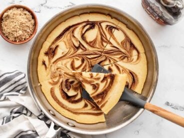 cinnamon swirl oven pancake with one slice on a spatula on the skillet