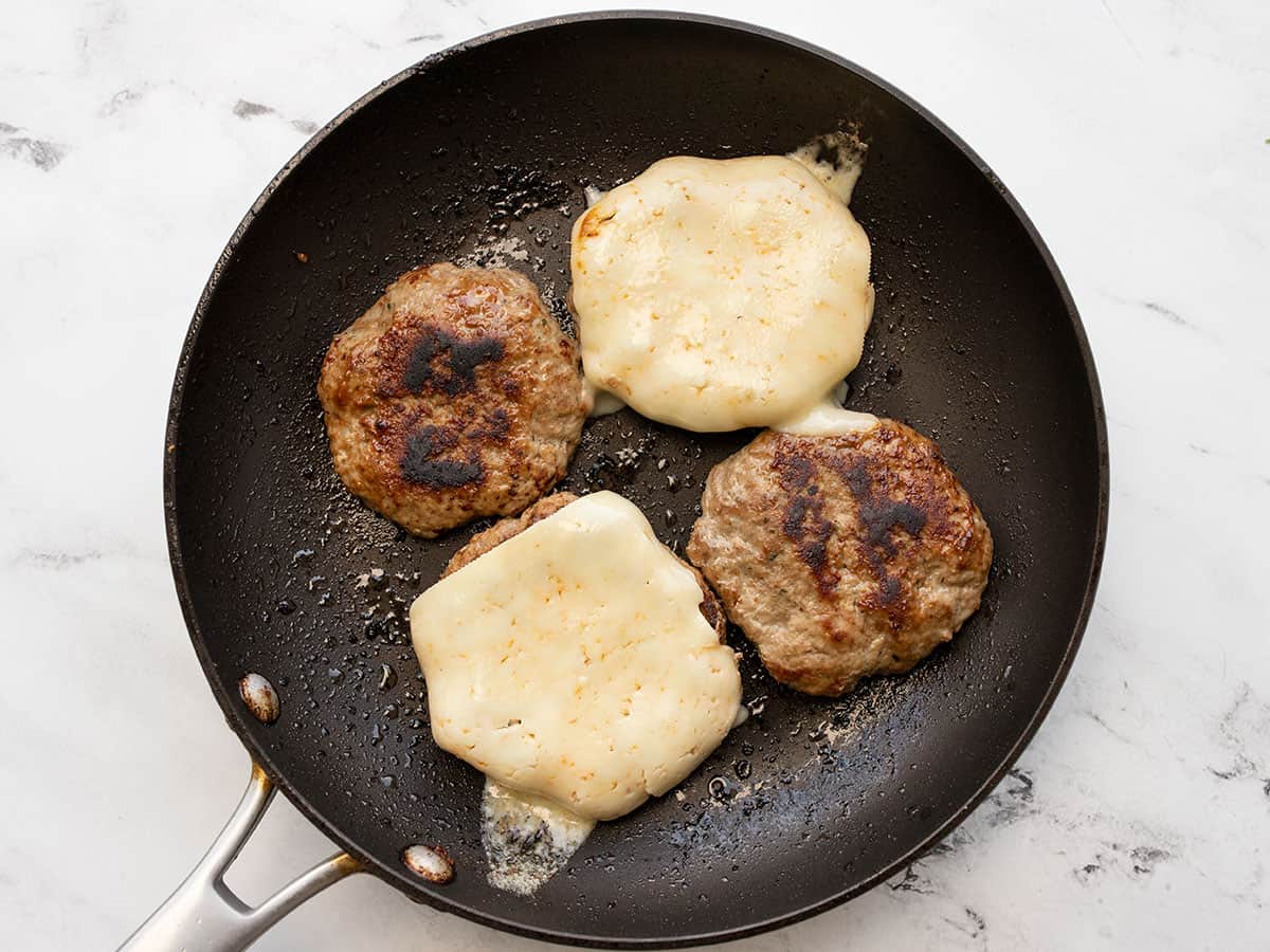 Cooked turkey burgers in a skillet, two with cheese on top