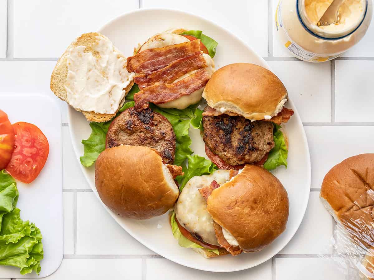 Burgers being assembled on a platter with ingredients on the sides