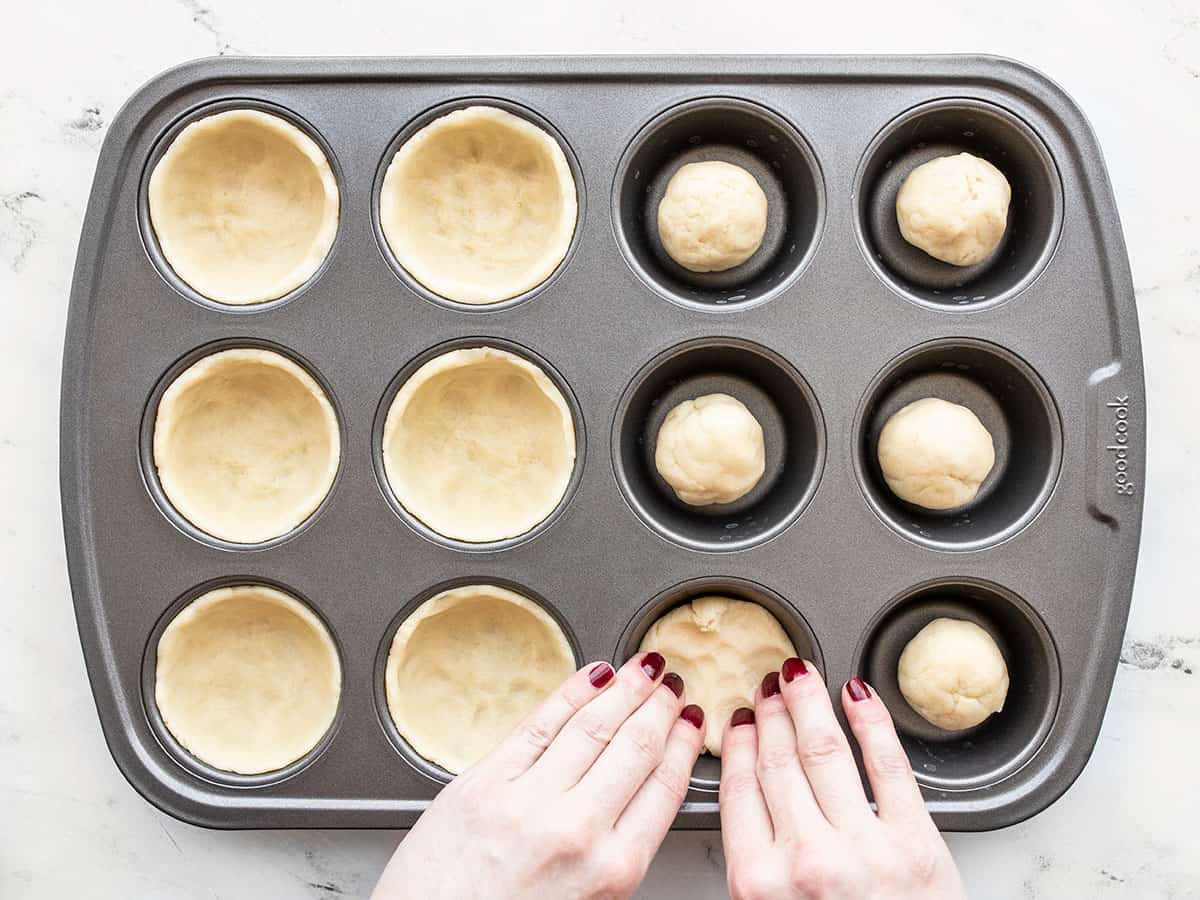 Dough being pressed into the muffin tin