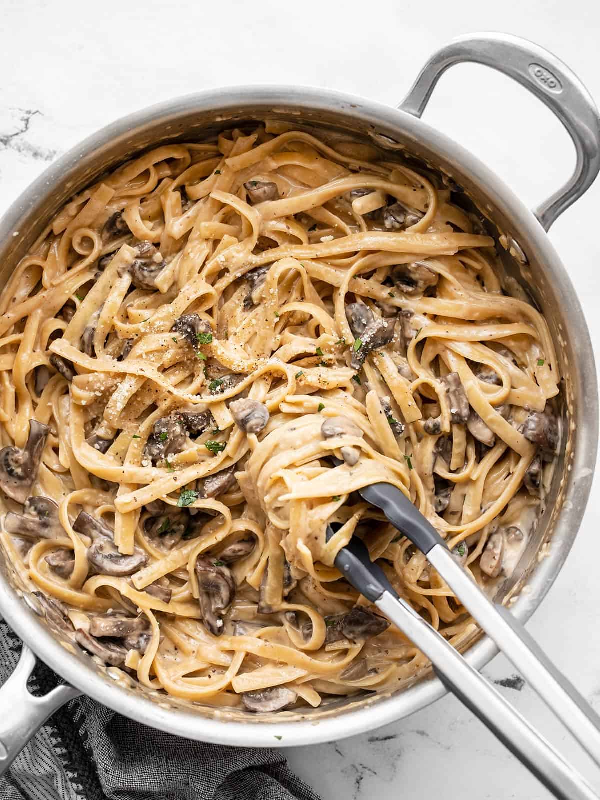 Pasta being twirled around tongs in the skillet