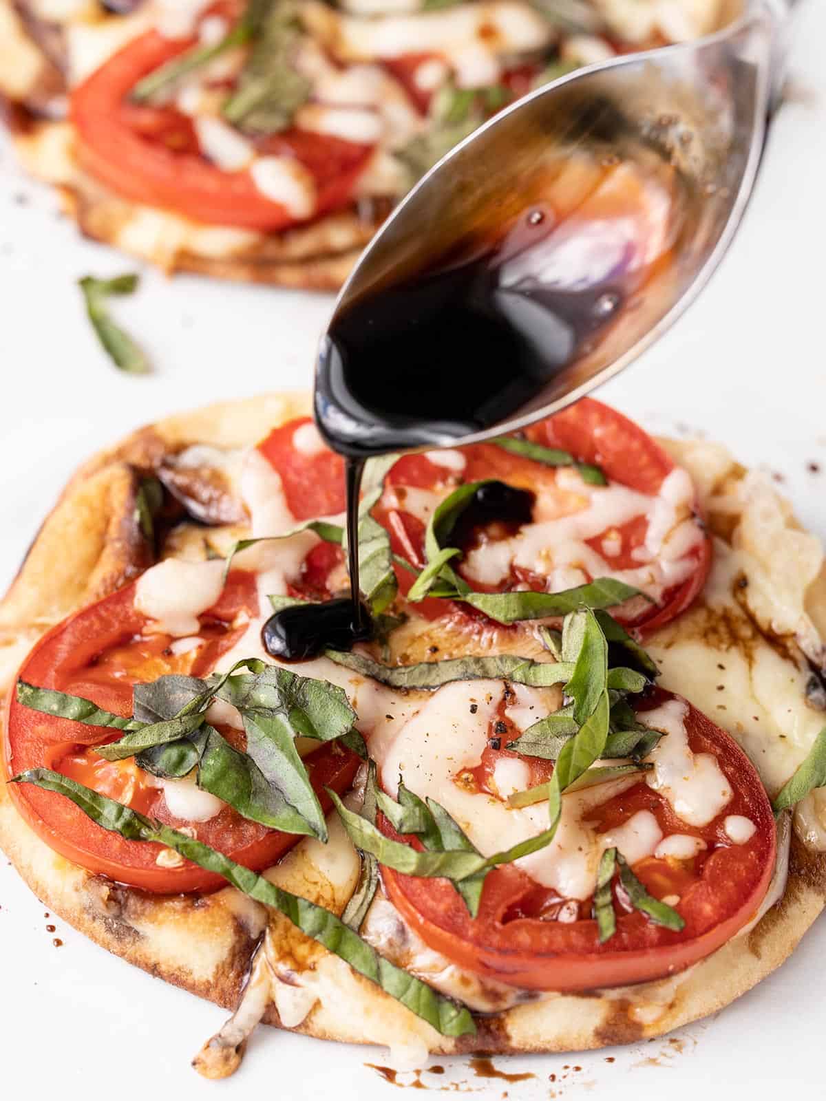 Balsamic reduction being drizzled over the caprese pizza