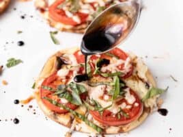 Balsamic reduction being drizzled onto a mini caprese pizza