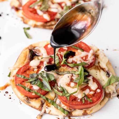 Balsamic reduction being drizzled onto a mini caprese pizza