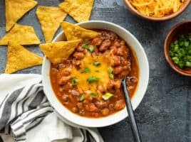 Overhead view of a bowl of pumpkin chili with cheese and tortilla chips