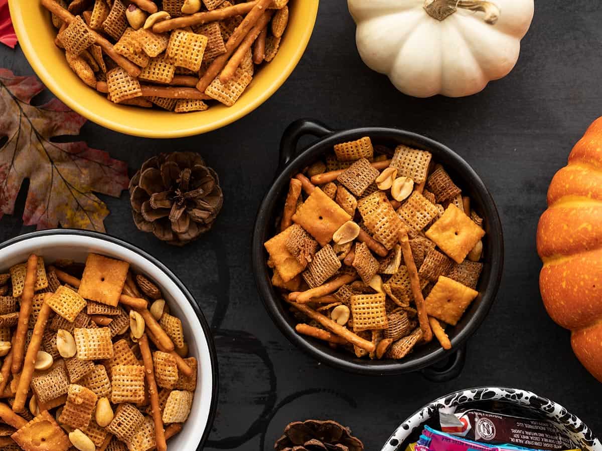 Three bowls of spicy chex mix with pumpkins on the sides