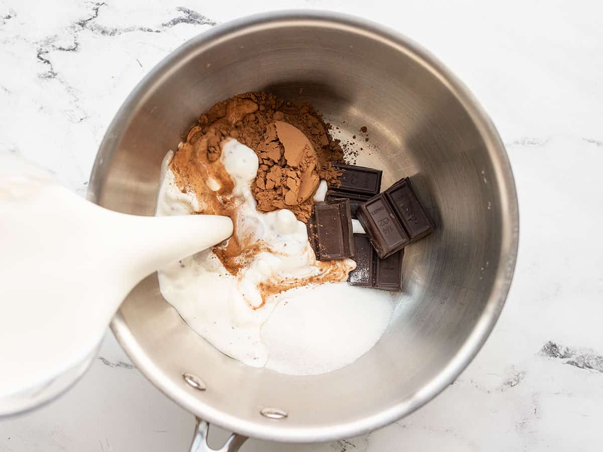 Milk being poured into a sauce pot with chocolate sugar and salt