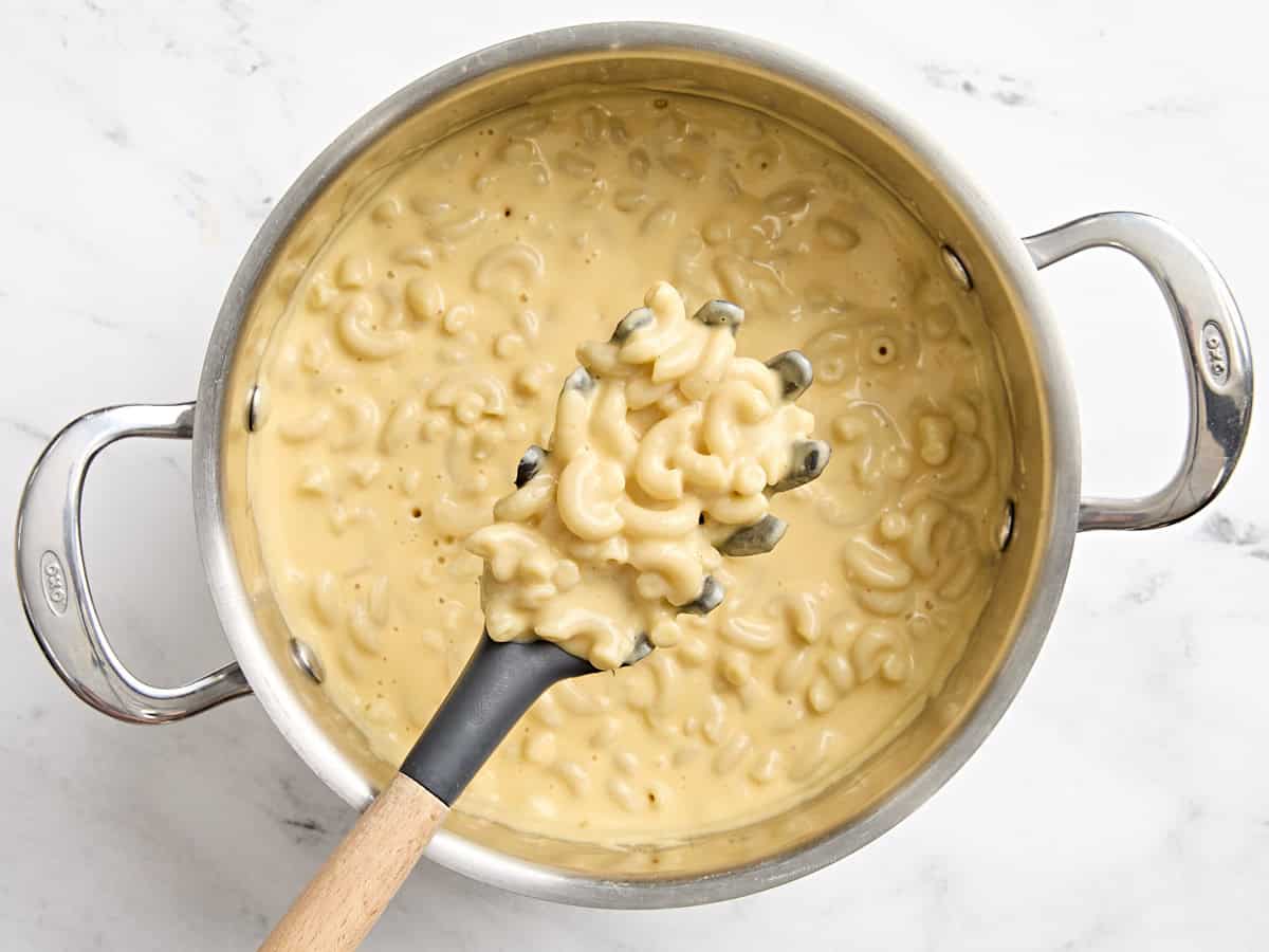 Overhead view of mac and cheese in a sauce pan with a slotted spoon.